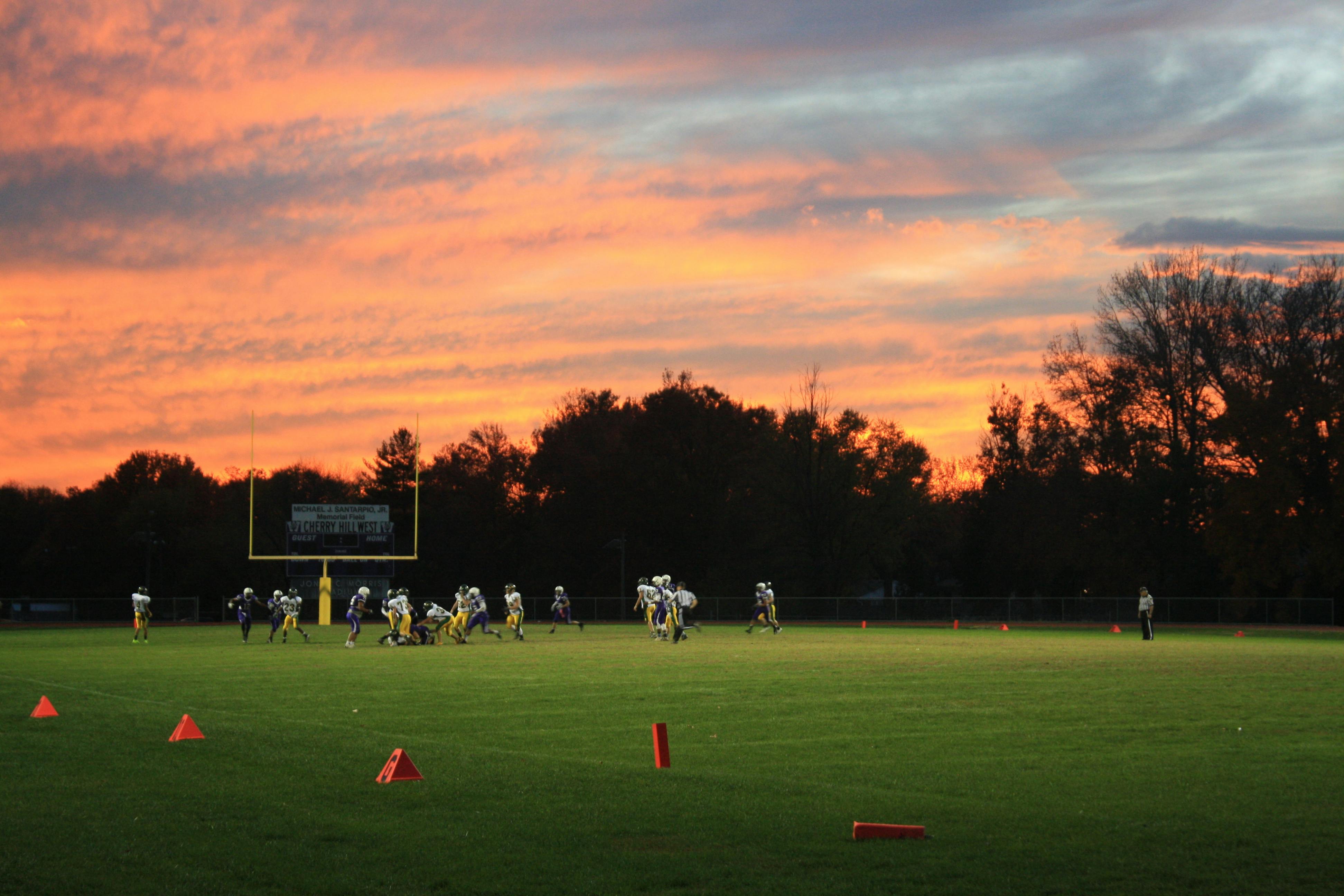 a football field with a team playing with a beautiful orange sunset
