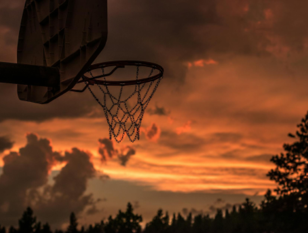 a silhouette of a basketball hoop with a sunset sky in the background