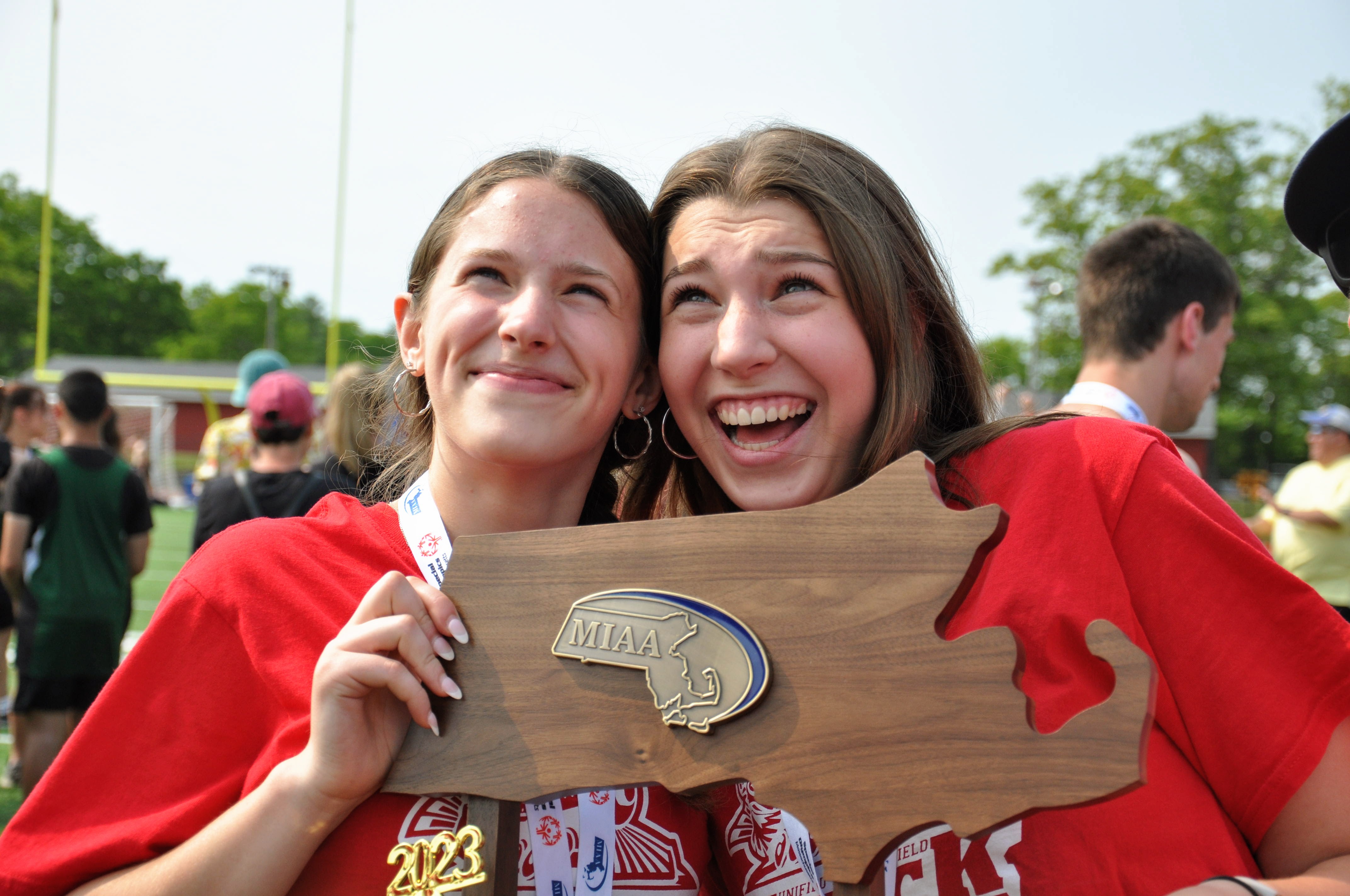 two women in red shirts hold an MIAA plaque 
